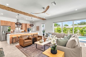A modern kitchen with a central island, a dining area with a sofa and coffee table, and a view of a swimming pool. - Waldemere's Wonderland (Sarasota)