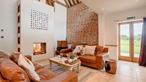 A spacious living room with a fireplace, leather sofas, a coffee table, and a brick wall. - 5 Bed in Ellough (oc-d8656) (Ellough)