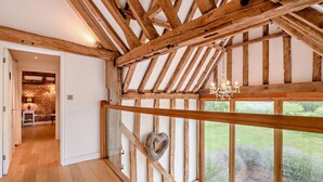 A room with exposed wooden beams, a wooden railing, and a view of a garden through large windows. - 5 Bed in Ellough (oc-d8656) (Ellough)