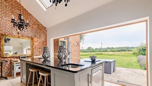 A modern kitchen with a large island, a brick wall, and a view of the countryside. - 5 Bed in Ellough (oc-d8656) (Ellough)