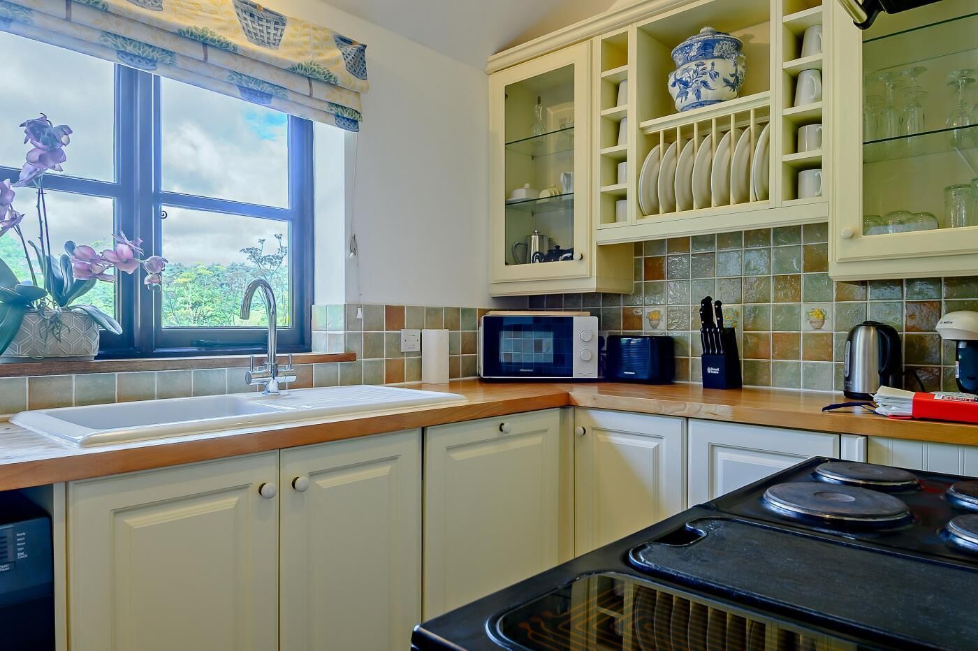 A kitchen with a window, a microwave, a stove, and a cabinet with dishes.