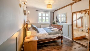 Ein Schlafzimmer mit einem Holzbett, Nachttischlampen, einem Fenster und Blick ins Badezimmer.