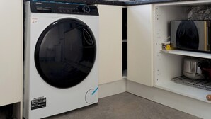 A compact washer and dryer unit in a kitchen with white cabinets and a black countertop.