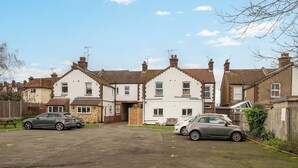 A residential street with two-story houses, parked cars, and a wooden fence.