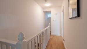 A staircase with white railings leading to a room with a door and a light switch on the wall.