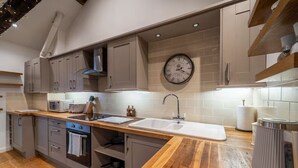 Une cuisine avec des meubles de couleur grise, un plan de travail en bois, un évier, une cuisinière et une horloge au mur.