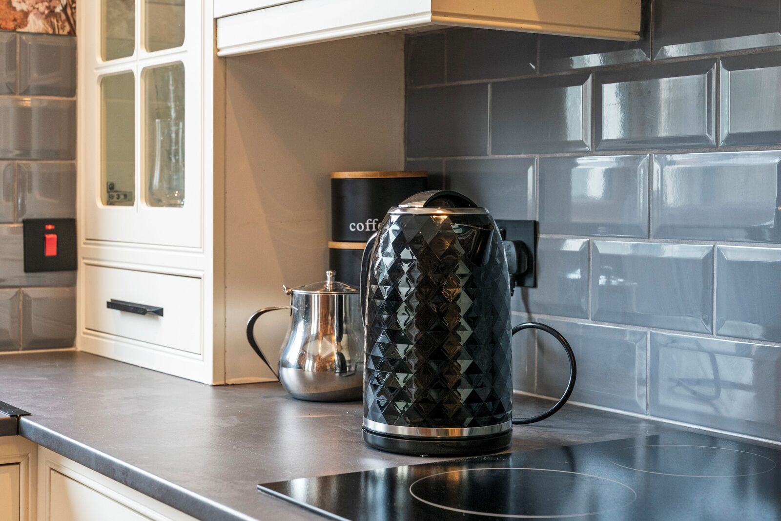 Une cuisine avec une machine à café sur le plan de travail, une bouilloire et une autre machine à café en arrière-plan.