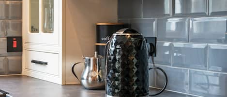 A kitchen with a coffee maker on the counter, a kettle, and a coffee machine in the background.