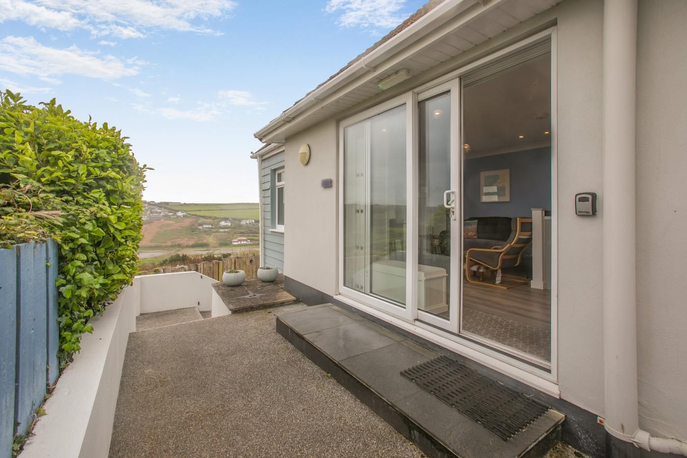 A modern building with a glass door entrance, a small outdoor seating area, and a view of the countryside.