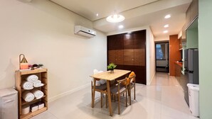 Un espacio habitable compacto con zona de comedor, un estante de madera con toallas, una mesita y una cocina con refrigerador.