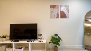 Una sala de estar con un televisor de pantalla plana sobre un soporte blanco, dos obras de arte abstracto en la pared, una planta en maceta y cajas de almacenamiento debajo del soporte.