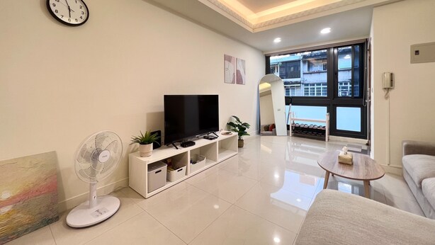 Una sala de estar moderna con un televisor de pantalla plana, un ventilador de pie y un espejo grande.