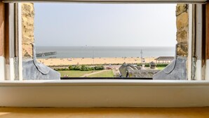 Blick durch ein Fenster mit Steinwänden, einem Strand und einem Pier in der Ferne.