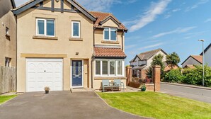 A two-story residential house with a front garage, a small patio with outdoor furniture, and a well-maintained lawn. - 4 Bed in Seahouses (oc-o27867) (Seahouses)
