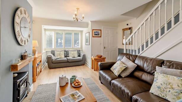 A cozy living room with a sofa, a brown leather couch, a fireplace, a wooden coffee table, and a large clock on the wall. - 4 Bed in Seahouses (oc-o27867) (Seahouses)
