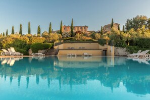 Una piscina con lettini, un edificio dalla facciata in pietra e vegetazione circostante.