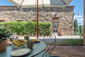 Un espace de restauration en plein air avec un mur en pierre en arrière-plan, une table sur laquelle se trouve un saladier rempli de fruits et un coin salon abrité.