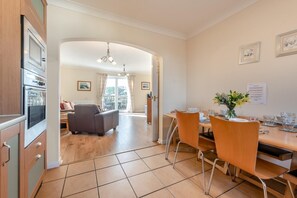 A modern kitchen with built-in appliances, a dining area with orange chairs, and a view to a balcony.