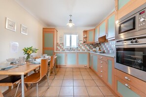 A kitchen with a dining table, chairs, cabinets, and two ovens.