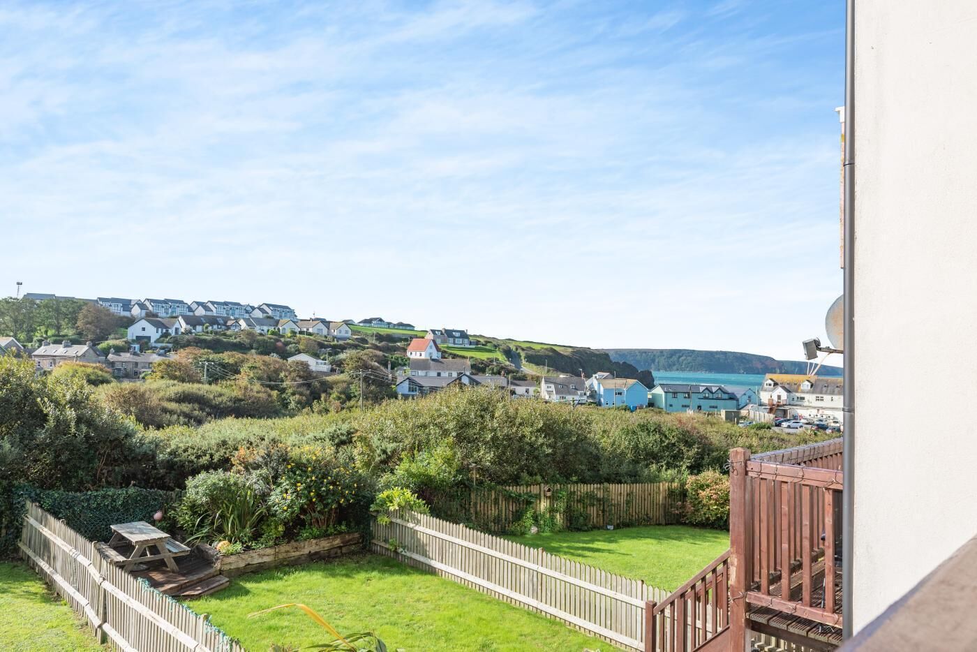 A coastal residential area with houses, a grassy yard, and a view of the sea.