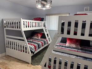 Ein Zimmer mit Etagenbetten, einem Fenster mit Jalousien und einer Deckenleuchte.