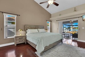 A bedroom with a bed, nightstands, a ceiling fan, and a view through an open door to an outdoor patio. - Tuscan Treasure Bike, Kayaks, Peddleboat Included (Cape Coral)