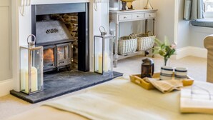 A cozy room with a fireplace, wicker baskets, and a table with candles and books. - 9 Bed in Instow (oc-a27886) (Instow)