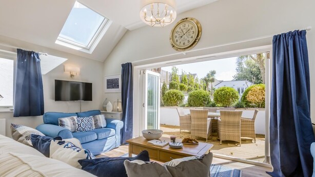 A modern living room with a sofa, coffee table, and TV. There is a balcony with outdoor furniture and a view of greenery. - 9 Bed in Instow (oc-a27886) (Instow)