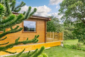 A wooden cabin with a window, a balcony, and a lush green garden. - 3 Bed in Llanddulas (oc-r27872) (Rhyd-y-foel)