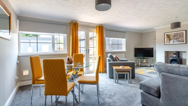 A modern living room with a glass dining table, yellow chairs, a grey sofa, and a television. - 2 Bed in Gimingham (oc-h27869) (Gimingham)