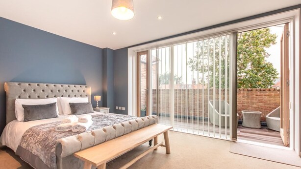 A bedroom with a large bed, a bench, a nightstand, and a view of the outside through a sliding glass door. - 2 Bed in Southwold (oc-t27861) (Southwold)