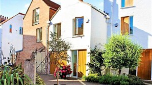 A row of residential buildings with a central white house featuring a wooden door and a small garden with a tree and flowers. - 2 Bed in Southwold (oc-t27861) (Southwold)