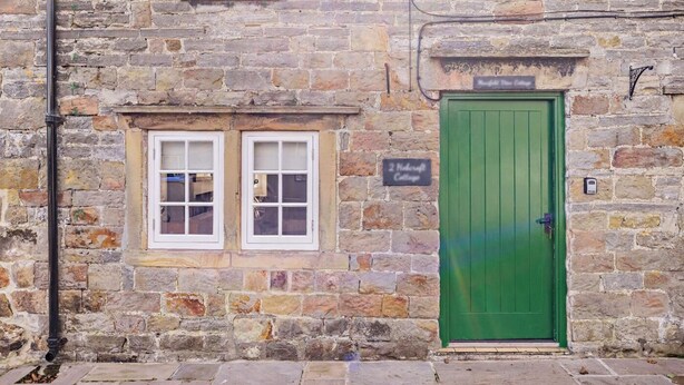 Un bâtiment en pierre avec une porte verte, deux fenêtres et une enseigne indiquant « 2 Middleton Cottages ».