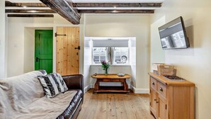 Une pièce chaleureuse avec un plancher en bois, une porte verte, un canapé en cuir marron, une table en bois ornée d’un vase et un buffet en bois.