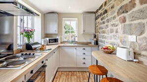 Une cuisine moderne avec un mur en pierre, des meubles blancs, un four à micro-ondes, un grille-pain et un plan de travail en bois.
