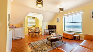 A spacious living room with a large window offering a view of the beach, a cozy seating area, and a dining space with a TV. - 2 Bed in Broad Haven (oc-s27911) (Broad Haven)