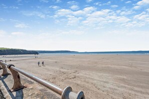 Ein weiter, sandiger Strand mit einer Metallreling im Vordergrund.