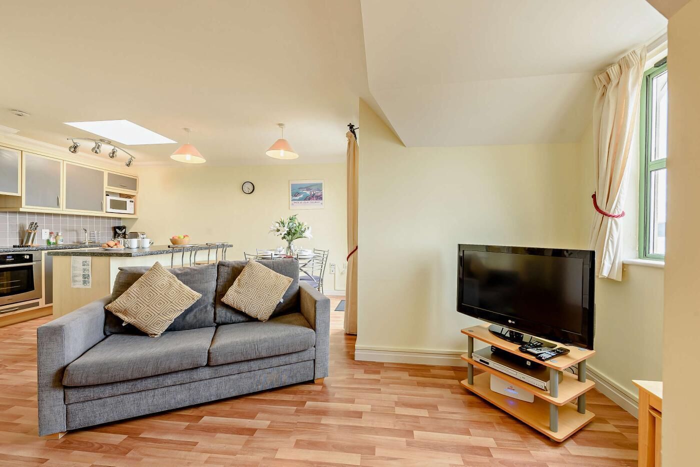 Een moderne woonkamer met een grijze bank, een flatscreen televisie en een houten tv-meubel.