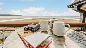 A table with binoculars, two mugs, a teapot, and a book with a photo, overlooking a beach. - 2 Bed in Broad Haven (oc-s27956) (Broad Haven)