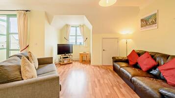 A living room with a sofa, a leather couch, a television on a stand, and a small table.