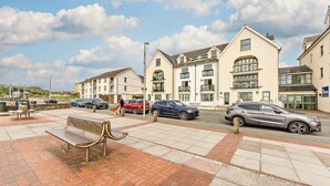 A coastal residential area with multi-story buildings, a paved walkway, and parked cars. - 2 Bed in Broad Haven (oc-s27956) (Broad Haven)