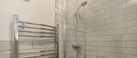 A bathroom with a glass shower enclosure, a chrome towel rack, and white tiled walls.