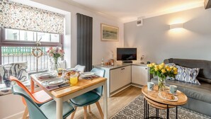Een moderne woonkamer met een eethoek, een bank, een televisie en een kleine keuken.