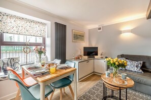 Una sala moderna con comedor, un sofá, un televisor y una pequeña cocina.