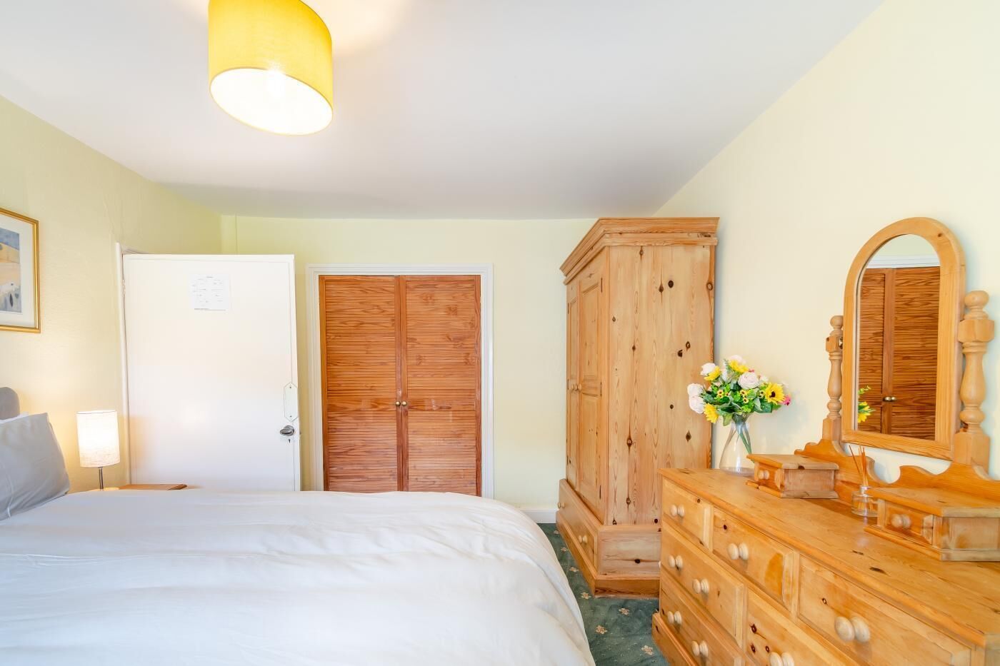 A hotel room with a bed, wooden wardrobe, dresser, and a mirror.