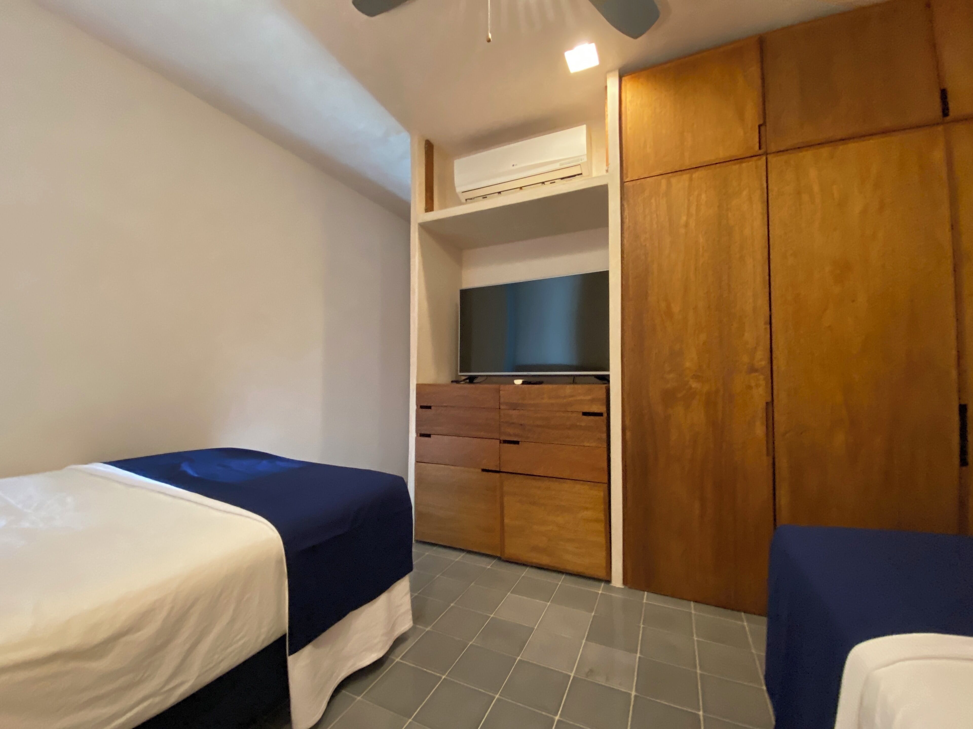 Camera da letto con due letti, televisione, armadio in legno e ventilatore a soffitto.