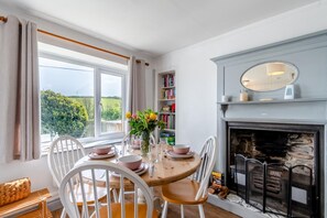 Ein Essbereich mit einem runden Tisch, weißen Stühlen, einem Kamin und einem Bücherregal.