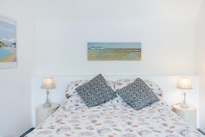 Ein Schlafzimmer mit einem Bett, zwei gestreifte Kissen, einem Bild an der Wand und zwei Nachttischlampen.