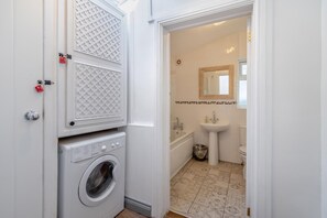 Ein Waschraum mit Waschmaschine und Trockner, einer kleinen Mülltonne sowie ein Badezimmer mit Waschbecken, Spiegel und Toilette.
