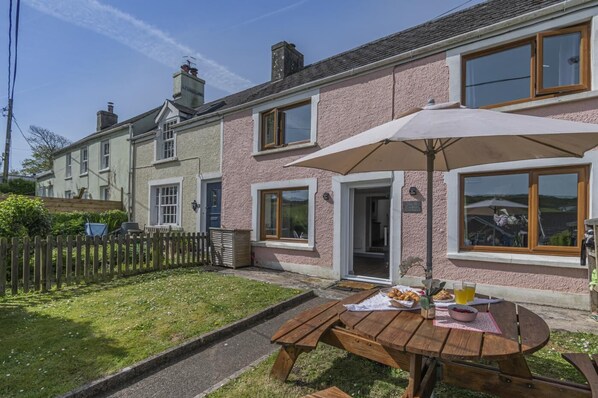 Ein zweistöckiges Haus mit Garten-Terrasse, inklusive Holztisch und Sonnenschirm.